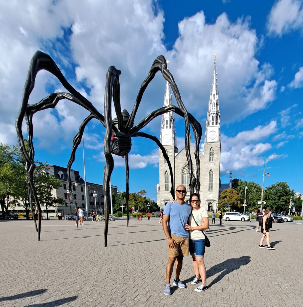 Rose e Vitor com a escultura Maman ao fundo, no centro de Ottawa.