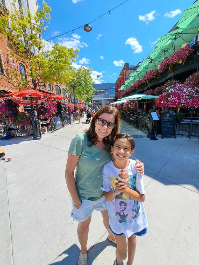 Rose e Luisa na William Street, com restaurantes com varandas floridas ao fundo.